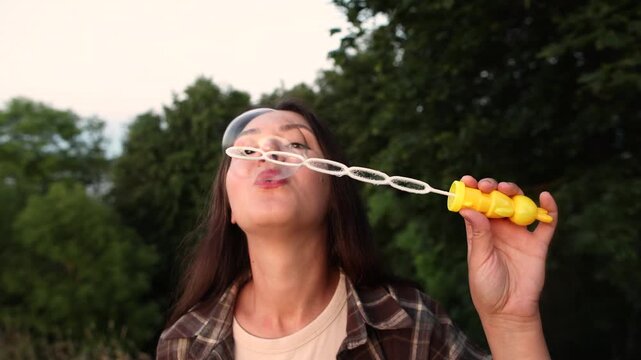 Young woman blows soap bubbles outdoors during evening light. Slow motion captures beauty relaxation and playful summer mood with dreamy atmosphere.