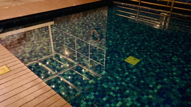 Reflective swimming pool with blue mosaic tiles and wooden deck