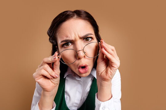Surprised young woman adjusting her glasses with a confused, skeptical expression in a close-up portrait on a neutral brown background