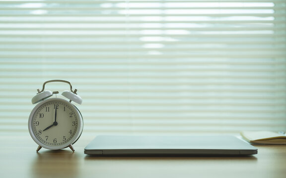 White alarm clock and closed laptop on desk. concept of starting work, morning productivity, time management and office hours with copy space.