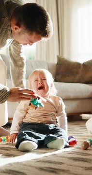 Baby boy, crying and father with toy for comfort or consoling on floor of home living room. Distraction, sad and tears of infant child in apartment with single parent man for care or development