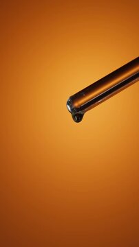 Close-up of transparent droplets on tip of glass rod on warm orange background