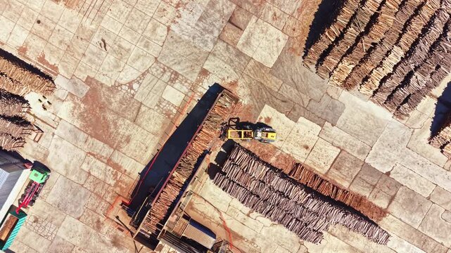 Aerial view of a lumber yard showing stacks of processed wood and machinery. Workers are handling logs and moving materials across the site.