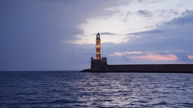 A cinematic view of the Venetian lighthouse standing proudly on the stone pier in Chania harbor, Crete