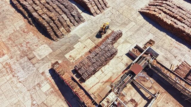 A large area shows stacked logs organized in rows while a machine operates on the site. This scene captures the wood processing activity in progress.