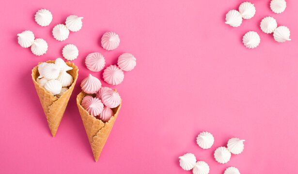 Ice cream cones with white and pink meringue on a pink background. Top view. Copy space.