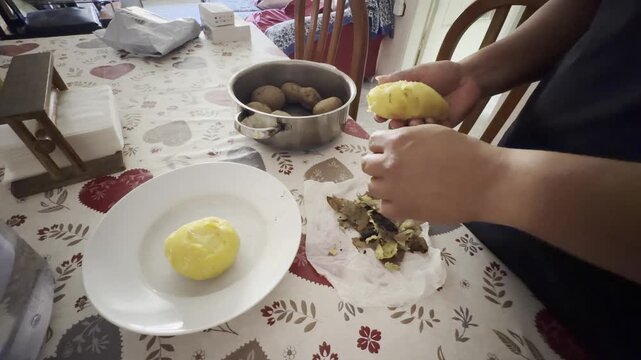Unrecognizable person peeling boiled potatoes on a plate in a domestic setting