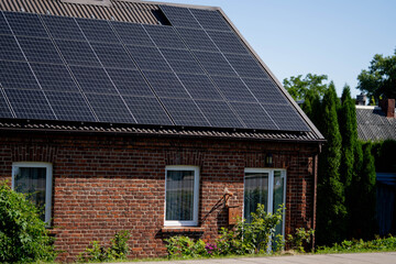 Fototapeta premium Solar panels installed on brick house roof with greenery and blue sky in background