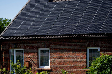 Fototapeta premium Solar panels installed on brick house roof with greenery surrounding the property