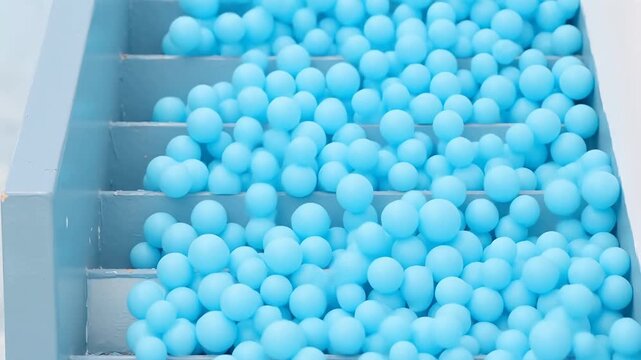 Blue spherical beads cascading down a tiered gray chute in slow motion