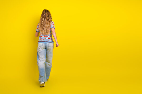 Young woman walking away on a bright yellow background in casual jeans and a patterned top, minimalist studio portrait conveying movement and carefree mood