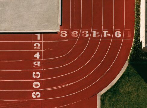 Aerial view of a red running track with white lane numbers curving into distance