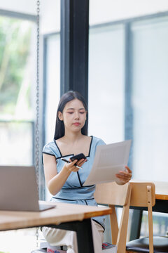 Businesswoman managing financial documents and reports, analyzing data using smartphone and laptop for remote work