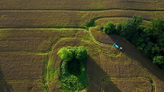 Red Tractor Towing Blue Sprayer Tank With Extended Boom Across Field in 4k