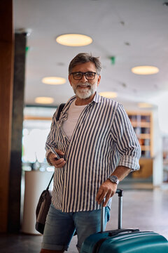 Happy mature man checking in at hotel and looking at camera.