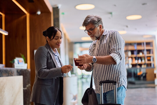 Happy female concierge assisting guest with checking in at hotel.