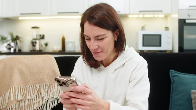 Young woman at home uses finance app on phone sees balance rise celebrates win raises fist. Caucasian girl on sofa sets new goal in phone notes tracks budget chart smiles success saving income profit