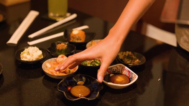 Hand Placing Small Plates of Japanese Izakaya Appetizers on Table