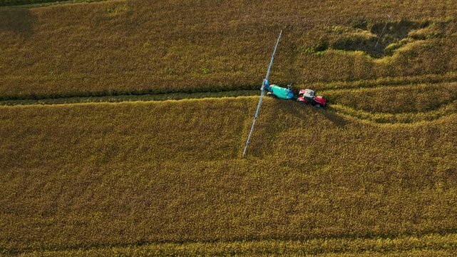 Tractor Towing Trailed Sprayer With Boom Arm Across Golden Field