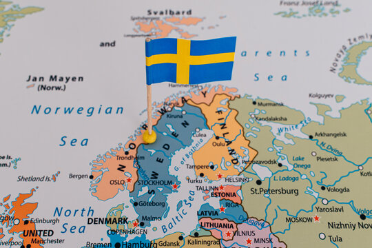 Close-up of a tiny Swedish flag pushpin marking Sweden on a political map, with Norway and Finland in focus, conceptualizing Scandinavian travel, food, and Northern European geopolitics.