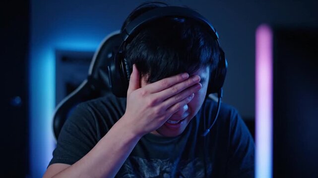Young gamer wearing a professional headset expressing disappointment and stress after losing a competitive online match.