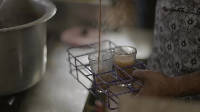 Indian Tea Vendor Filling Glass Cups with Hot Masala Chai During Monsoon