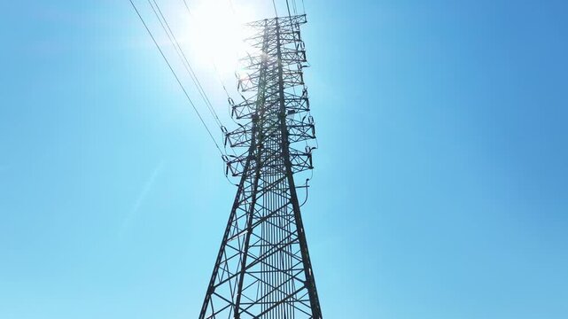 High voltage transmission tower captured from low angle against clear blue sky with bright sunlight