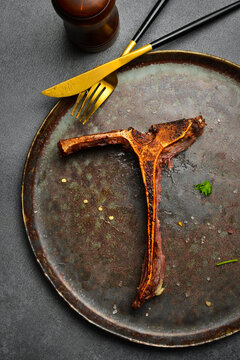Empty T-bone steak bone left on a vintage metal plate with salt. The delicious beef dinner is completely eaten. Perfect background for steakhouse menu design.