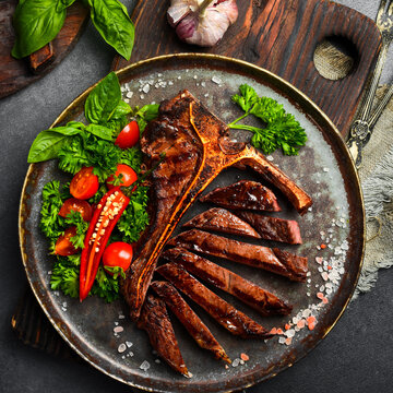 Sliced grilled T-bone steak served on vintage metal plate with tomatoes and basil. Premium beef dish with spices. Perfect background for steakhouse menu design.