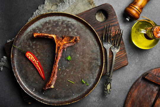 Clean Porterhouse steak bone rests on a dark dish with spices and vintage forks. High quality grilled meat was thoroughly enjoyed. Great image for restaurant.