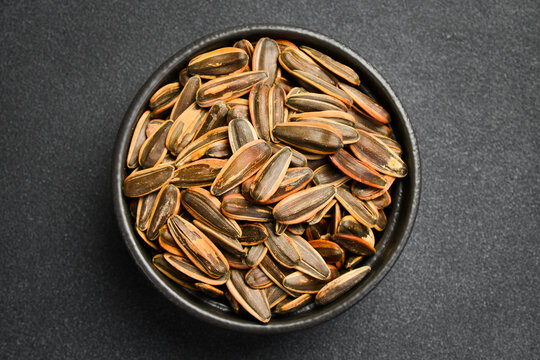 Roasted striped sunflower seeds in shell served in a black bowl. Healthy organic snack rich in protein. Perfect choice for food product packaging design.
