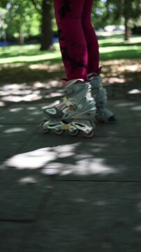 Vertical screen close up of female legs pushing forward on roller skates along a shaded park path showing active footwork motion and smooth recreational skating outdoors
