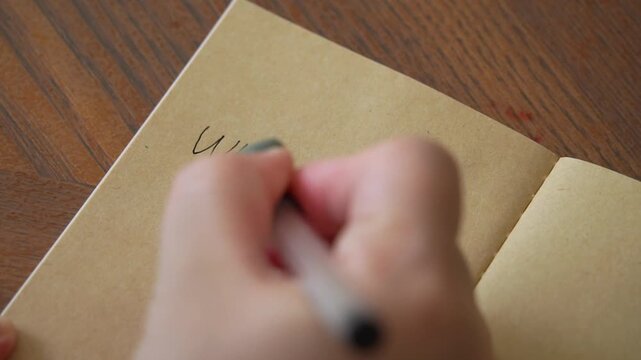 4K video of woman hand writing down in vintage notebook. Person writing in a gratitude journal with black ink, focusing on mindfulness and reflection.