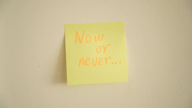 Hand Placing "now or never" Sticky Note on Wall