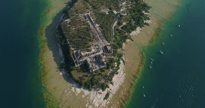 Stunning drone video sweeps over the rocky Hel Peninsula tip, revealing ancient ruins, lush greenery, vivid turquoise shallows, and boats dotting the serene coastline in daylight aerial footage.