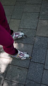 Vertical screen close up view of female rollerblades gliding over a paved path showing footwork balance and motion during an active summer skating session outdoors in sun
