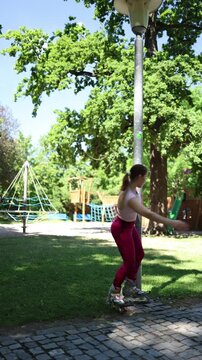 Vertical screen playful woman spins around a lamp post on rollerblades turning her park workout into a funny carefree moment while enjoying summer skating and outdoor fun