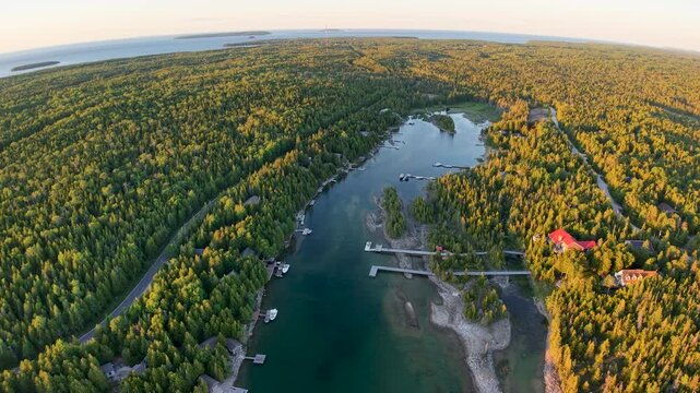 Drone looks along a long sheltered harbor bordered by forest and rocky Tobermory shoreline