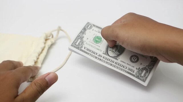 Close-up Hand Arranging Stacks of Cash Money and Putting Dollars into a Small Canvas Drawstring Bag on Plain White Background