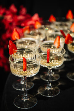 Close-up of elegant champagne coupes garnished with fresh strawberry slices. A sophisticated detail for a luxury wedding reception or festive celebration event.