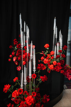 Decor. Closeup of elegant floral decor, featuring vibrant red flowers and tall glowing candles against a dramatic black backdrop. Perfect for wedding, birthday, or festive events.