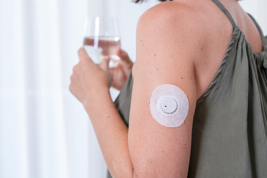Woman with glucose sensor on arm drinking water at home