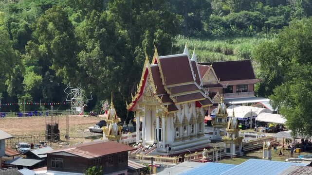 Wat Sri Kaew ordination hall in Nong Bua Lamphu, Thailand, surrounded by village houses, lush trees, and a riverside community in Nov 2023.
