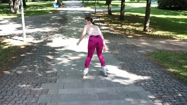Woman practices basic inline skating with an unstable stance and wide leg position while learning to control speed and maintain balance on a park pathway