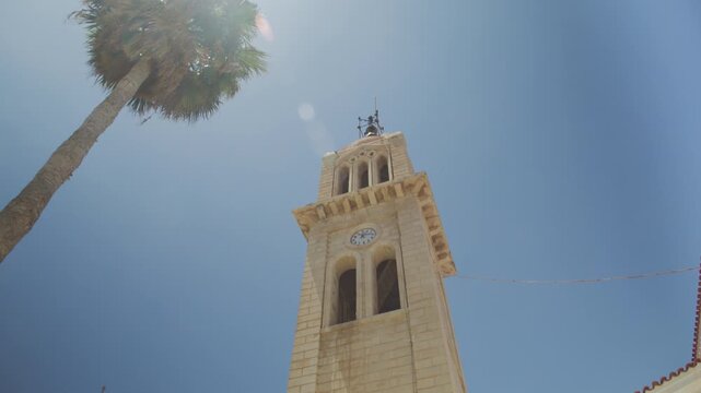 Shot of the historic Megalos Antonios church bell tower and a palm tree under a sunny blue sky in Rethymno.
