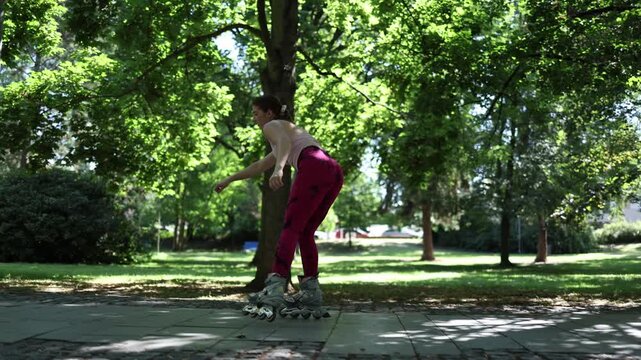 Woman practices inline skating for the first time moving carefully with uncertain balance and beginner technique while learning basic roller skills in a sunny park