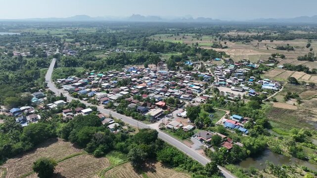 Drone view of Wat Sri Kaew surrounded by a rural community, riverside scenery, lush trees, and village houses in Nong Bua Lamphu, Thailand, Nov 2023
