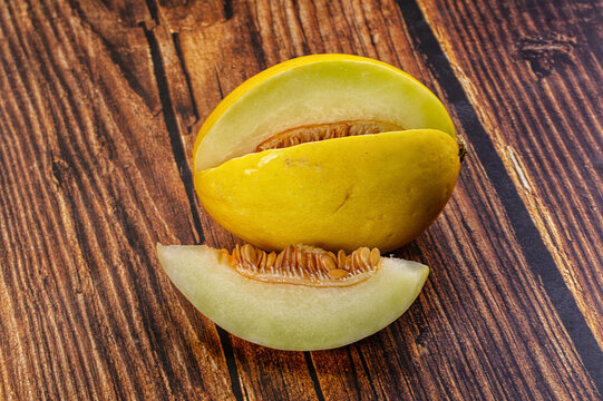 Fresh ripe yellow melon cut open with slice and seeds on dark wood surface