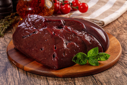 Raw beef liver on wooden board with basil and cherry tomatoes