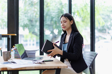Asian businesswoman organizing her schedule with a notebook and pen, working at an office desk